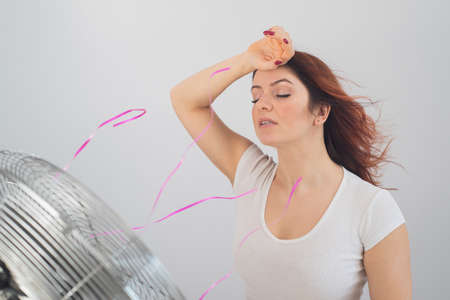 Joyful caucasian woman enjoying the wind blowing from an electric fan on a white background.の写真素材