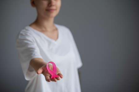 A faceless woman wearing a white t-shirt holds a pink ribbon as a symbol of breast cancer on a white background.の写真素材