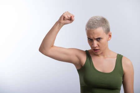 Young caucasian woman holding her fist up on a white background. A girl with short hair is fighting for rightsの写真素材