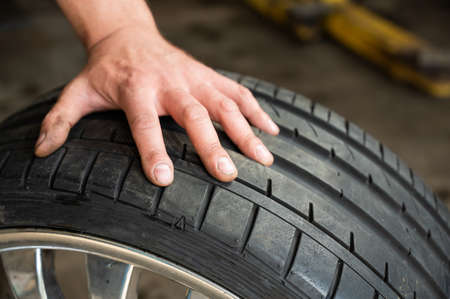 An auto mechanic holds a wheel of a car. Change of car tires according to the season