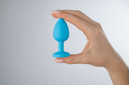 Woman holding a blue butt plug on a white background. Adult toy for alternative sexの写真素材