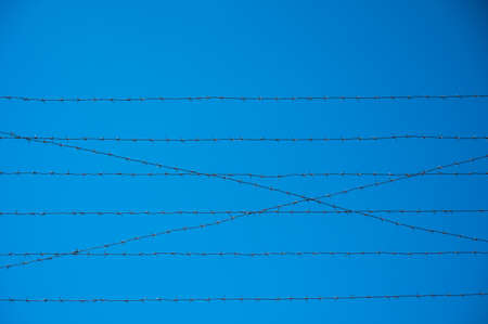 Barbed wire on the fence of the prison against the blue sky