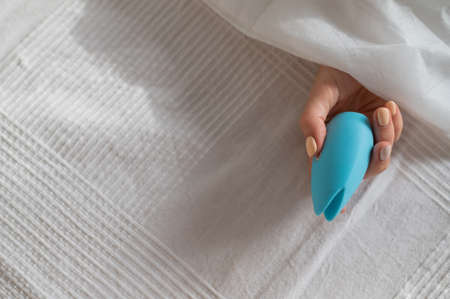 A faceless woman lies in bed under a blanket holding a clitoral vibrator. The girl masturbatesの写真素材