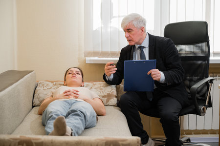 Caucasian woman lies on a couch at a reception with a psychotherapist. An elderly man works as a psychiatristの写真素材