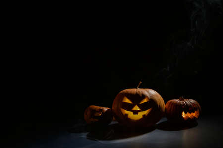 Pumpkins with carved grimaces and candles inside in the dark for halloween. Jack o latern in smoke.の写真素材