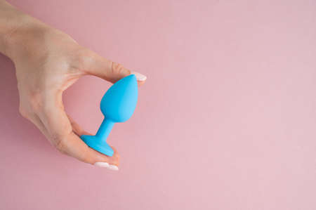 A woman is holding a blue butt plug on a pink background. Adult toy for alternative sexの写真素材