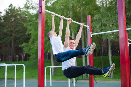 Caucasian man trains a boy on the horizontal bar on the playground. Dad and son go in for outdoor...