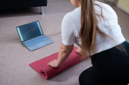 Young chubby woman folds sports mat after online fitness classの写真素材