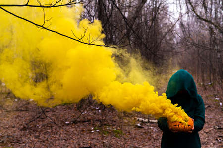 A creepy witch holds a steaming pumpkin in a deep forest. Jack o lantern emits yellow smoke for halloweenの写真素材