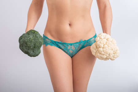 A faceless woman in panties holds cauliflower and broccoliの写真素材