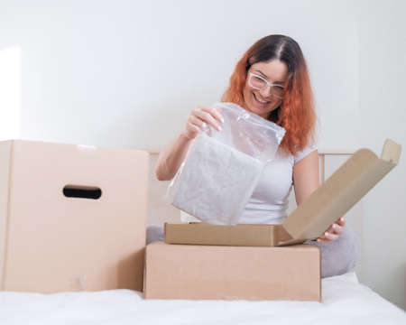 Caucasian woman opens an order while sitting in bed. Online shopping concept with home delivery