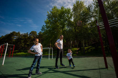 Caucasian man and two boys doing exercises outdoors. Father and sons train on the sports groundの写真素材
