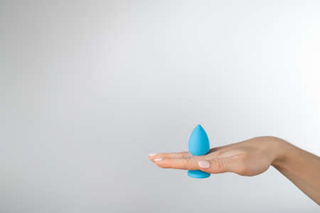 Woman holding a blue anal plug on a white background. Adult toy for alternative sexの写真素材