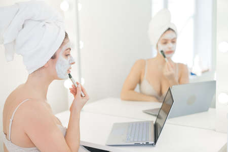 Caucasian woman applying face mask and looking at laptop manual.