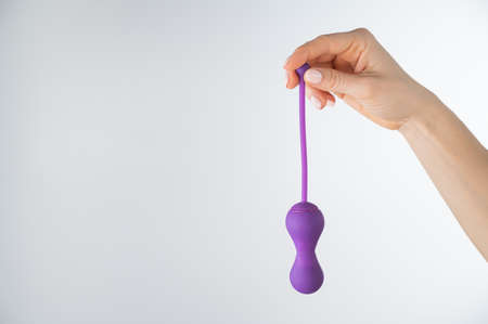 A faceless woman holding an electronic Kegel trainer for training pelvic floor muscles on a white...