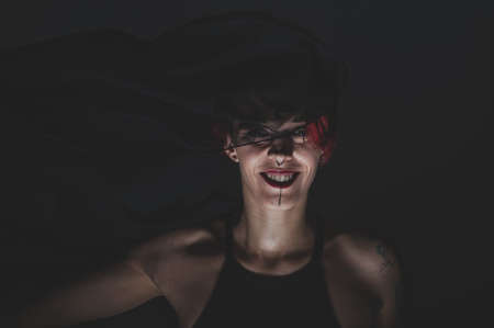 Redhead woman with a black veil on her head in a dark studio. A girl with an earring in her nose smiles slyly. Witch Makeup. Halloween costume.の写真素材