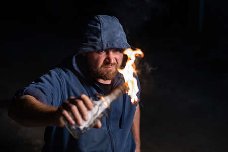 The man in the hood is holding a burning bottle. Molotov cocktail.