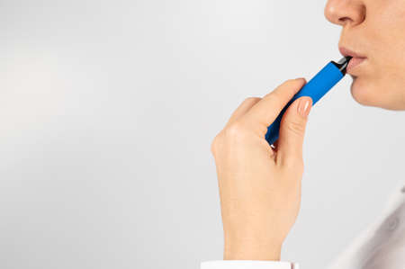 Caucasian woman smokes disposable vape on white background. Alternative device for smoking.
