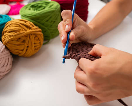 Close-up of a woman crocheting a basket of cotton yarn.