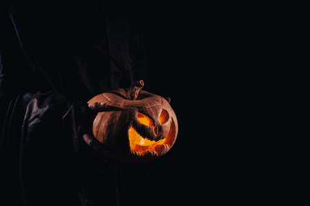 The witch is holding a pumpkin jack o lantern glowing in the dark. Halloween.