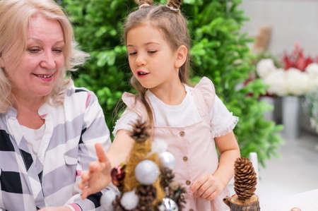 Elderly caucasian woman making pine cones decoration for christmas with two granddaughtersの写真素材