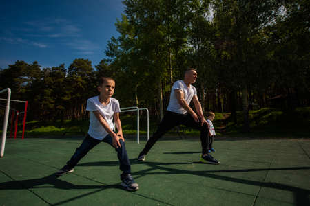 Caucasian man and two boys doing exercises outdoors. Father and sons train on the sports groundの写真素材