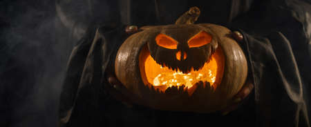The witch is holding a pumpkin jack o lantern glowing in the dark. Halloween.の写真素材