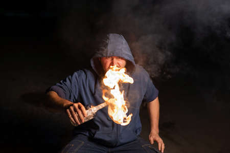 The man in the hood is holding a burning bottle. Molotov cocktail.の写真素材