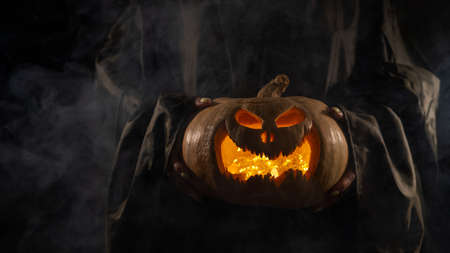 The witch is holding a pumpkin jack o lantern glowing in the dark. Halloween.の写真素材
