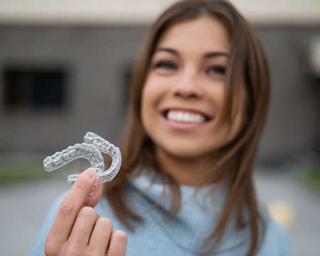 Caucasian woman with white smile holding transparent removable retainer. Bite correction device.の写真素材