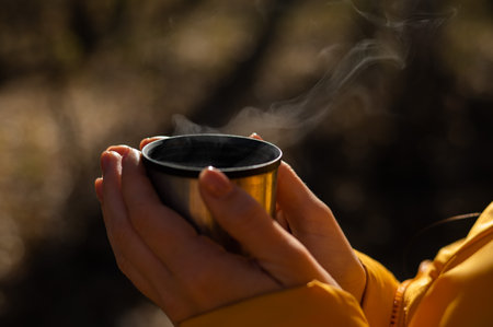 A woman holds a thermal cup of hot tea in her hands on a cold autumn day.の写真素材