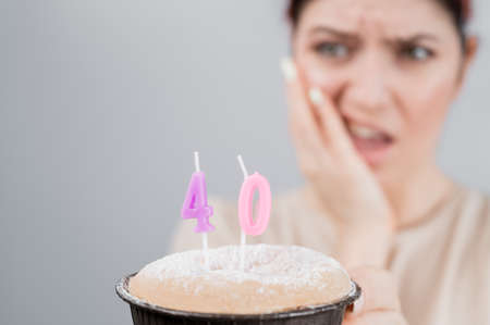 Unhappy woman holding a cake with candles for her 40th birthday. The girl cries about the loss of...