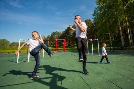 Caucasian man and two boys doing exercises outdoors. Father and sons train on the sports groundの写真素材