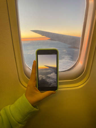 Caucasian woman photographs by smartphone the sky in the airplane window.の写真素材