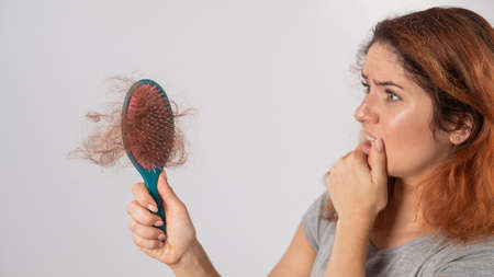 Caucasian woman with a grimace of horror holds a massage comb with a bun of hair. Hair loss and female pattern baldness.の写真素材