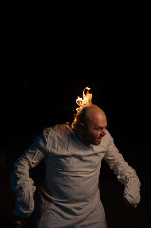 Bald man in a straitjacket with a burning head on a dark background.の写真素材