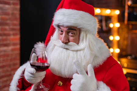 Santa claus with a glass of red wine wishes merry christmas and says toastの写真素材