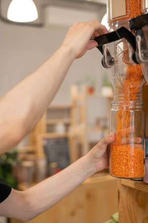 A man fills a jar with red lentils. Selling bulk goods by weight in an eco store. Trade concept without plastic packagingの写真素材