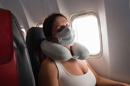 Caucasian woman on board aircraft in medical mask sleeping with neck pillow.の写真素材