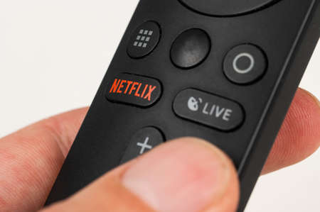 Russia, Novosibirsk 10.11.2021: Close-up of a man holding a black remote control with a netflix button on a white table.のeditorial素材