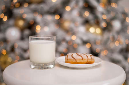 A glass of milk and a donut for santa claus on the background of a christmas treeの写真素材