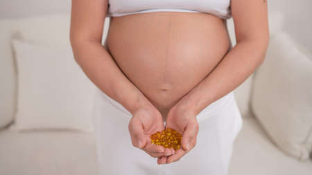 A pregnant woman with a bare belly holds a handful of vitamins. Transparent golden pills. Vitamin D for the expectant mother.の写真素材