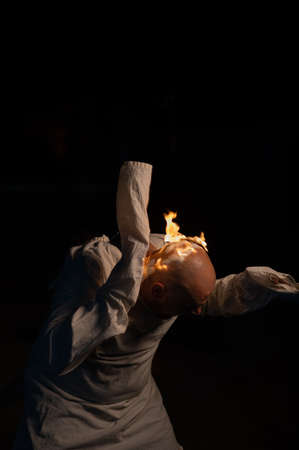 Bald man in a straitjacket with a burning head on a dark background.の写真素材