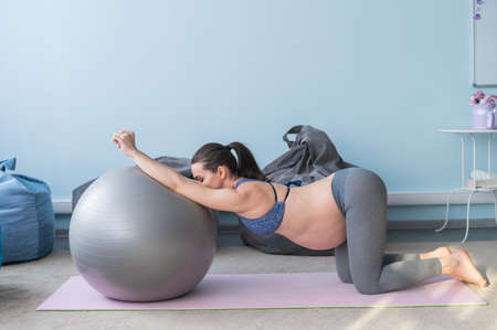 Pregnant european woman performs exercises with fitness ball. Expectant mother is doing yoga in the 3rd trimester. Girl in the classroom in preparation for childbirth.の写真素材