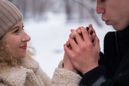 A young couple walks in the winter in the forest. The guy warms the girls hands.の写真素材