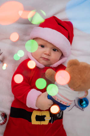 A baby boy dressed in a santa suit lies on the bed and plays with a Christmas garland.の写真素材