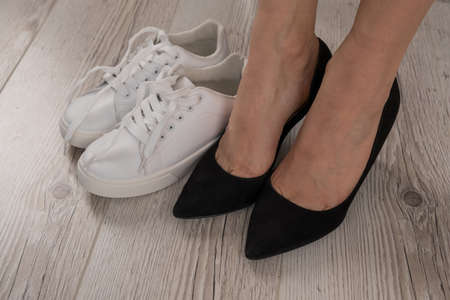 Close-up business woman takes off her shoes puts on white leather sneakers.