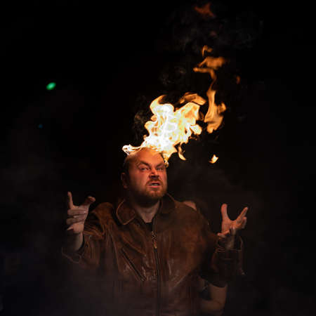 Bald man in a leather jacket with a burning head on a dark background.