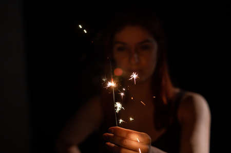 Caucasian woman holding sparkler in the dark.