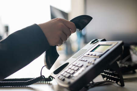 Close-up of the hand of a female office worker dialing a number on a landline phone. Faceless woman secretary calls on the phoneの写真素材